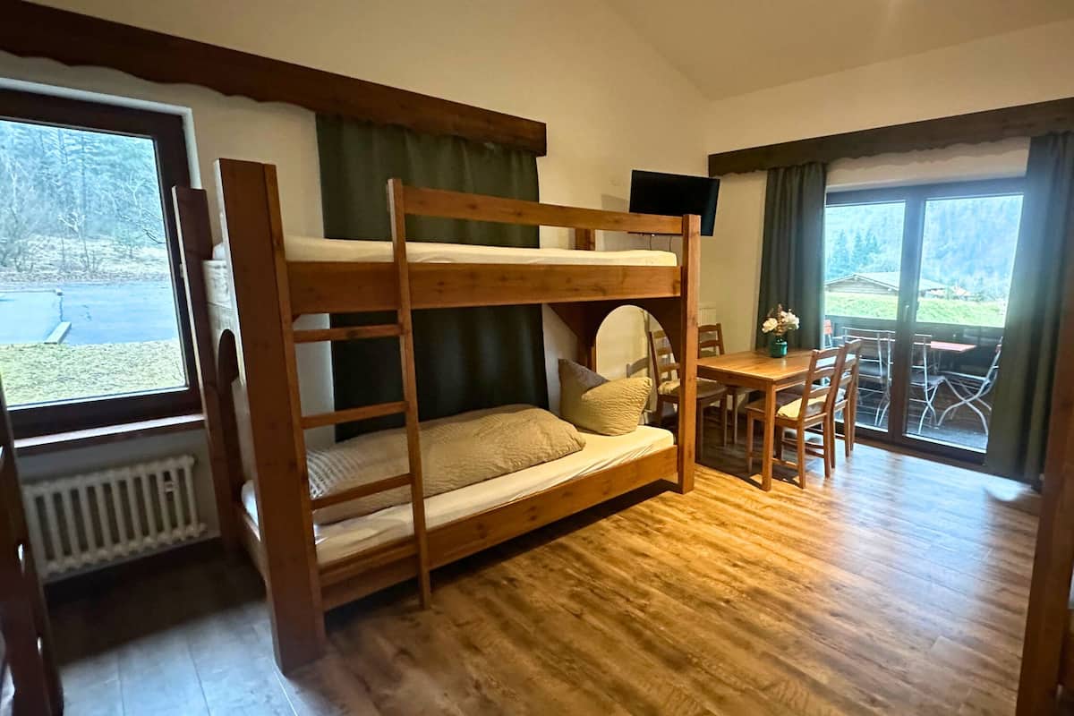 A room with bunk beds, a dining table with chairs, and large windows offering a view of the outdoors.