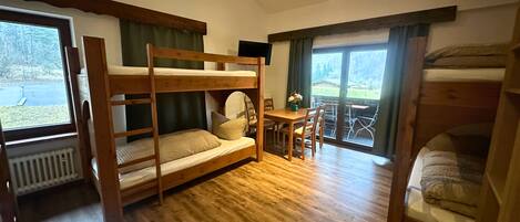 A room with bunk beds, a dining table with chairs, and large windows offering a view of the outdoors.