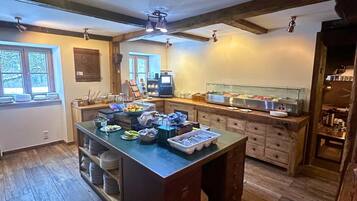 A kitchen with wooden floors, a central island with food items, a coffee machine, and a glass display case.