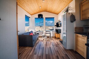 A modern interior with a wooden ceiling, a dining area with a table and chairs, a sofa with cushions, and a kitchen with cabinets and a refrigerator. - Blue View Cabin 6B with Hot Tub (Bláskógabyggd)