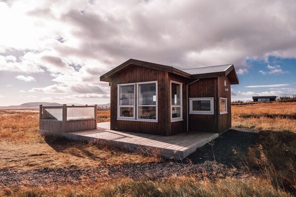 A wooden cabin with large windows, a deck, and a view of the surrounding landscape. - Blue View Cabin 6B with Hot Tub (Bláskógabyggd)