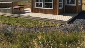 A wooden cabin with large windows, a deck, and a view of the landscape. - Blue View Cabin 6B with Hot Tub (Bláskógabyggd)