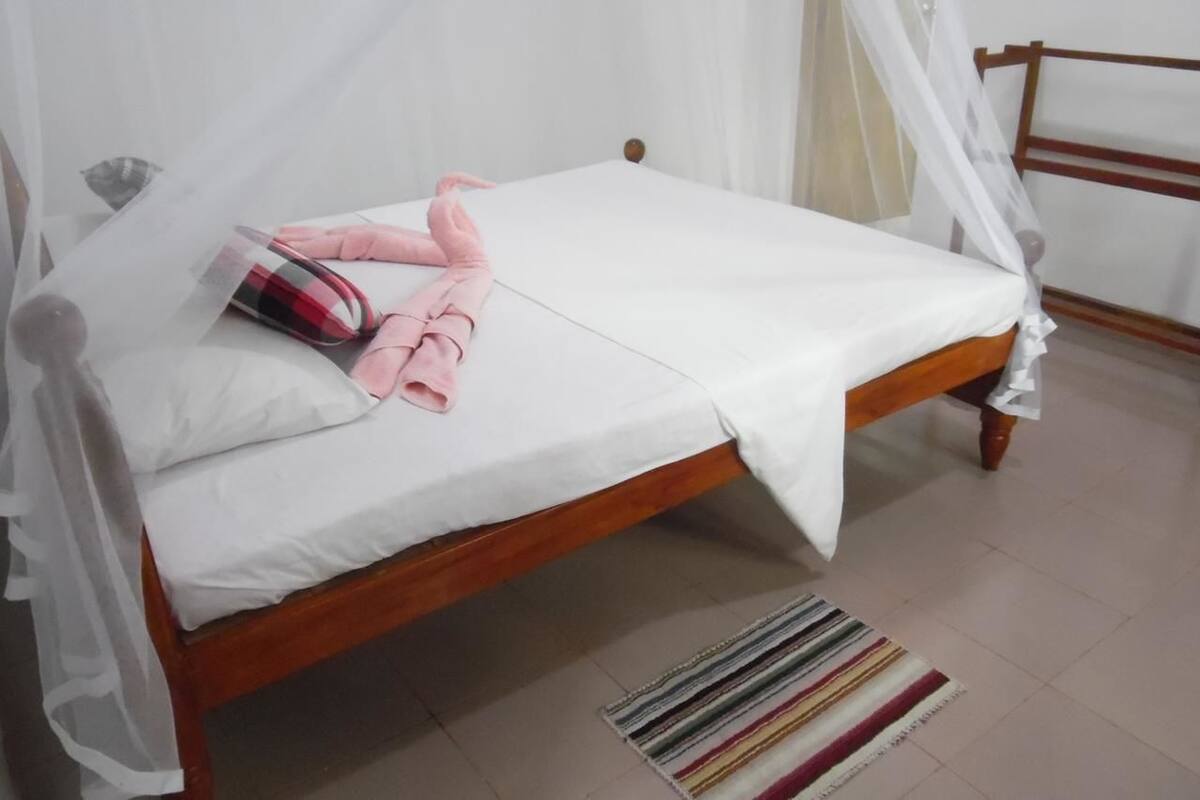 A neatly made bed with a white sheet and a pink towel, a wooden headboard, and a striped rug on the floor.