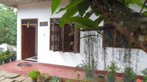 A building with a white exterior, a red base, and a door with a window. There are potted plants around the entrance. - Mango House (Talalla)