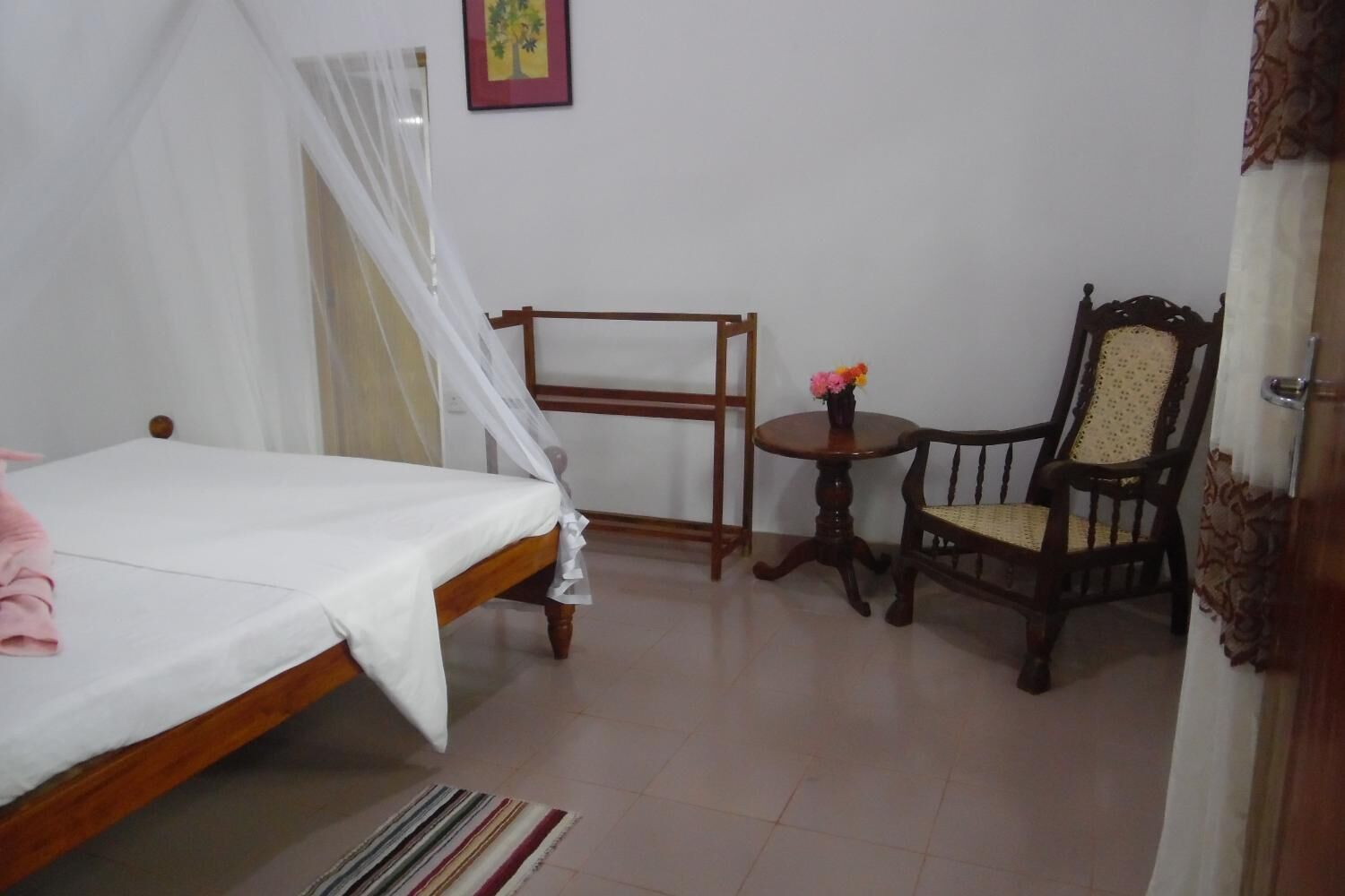 A bedroom with a bed, a chair, a small table with flowers, and a picture on the wall.