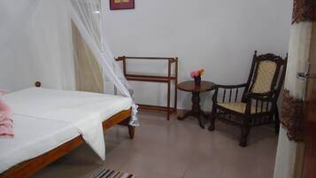 A bedroom with a bed, a chair, a small table with flowers, and a picture on the wall.