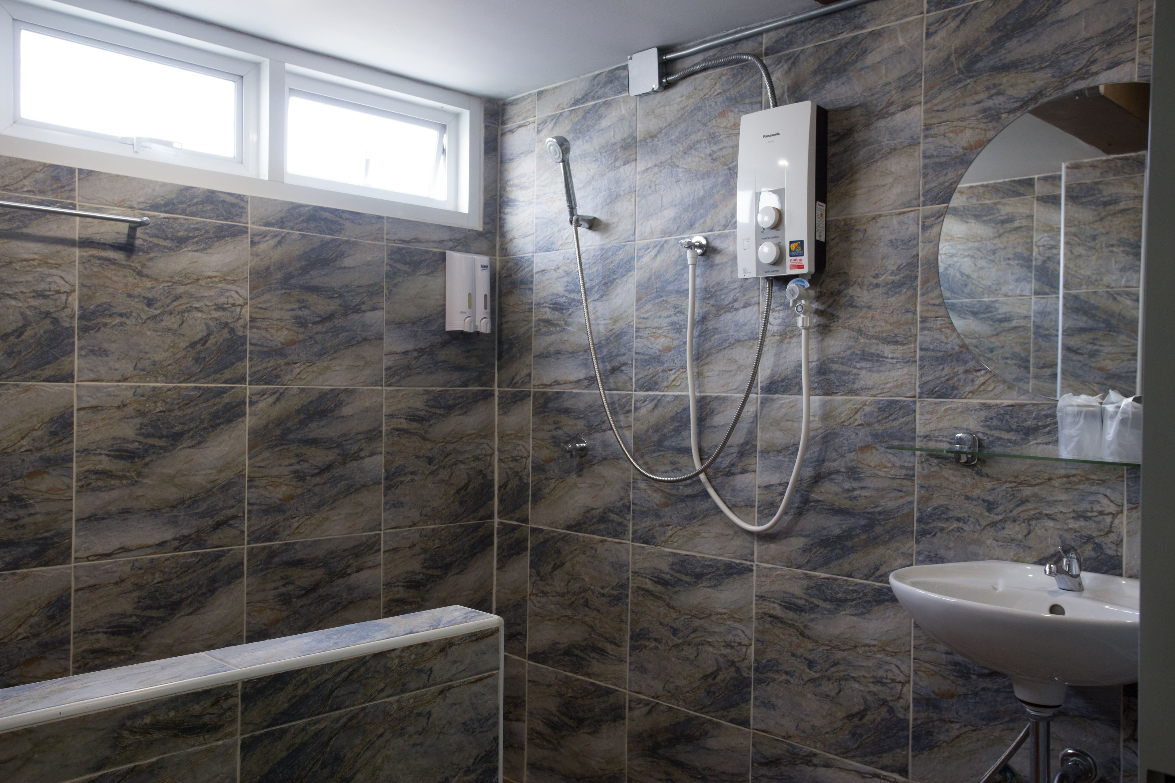 A bathroom with a marble tile wall, a shower, a sink, and a window.