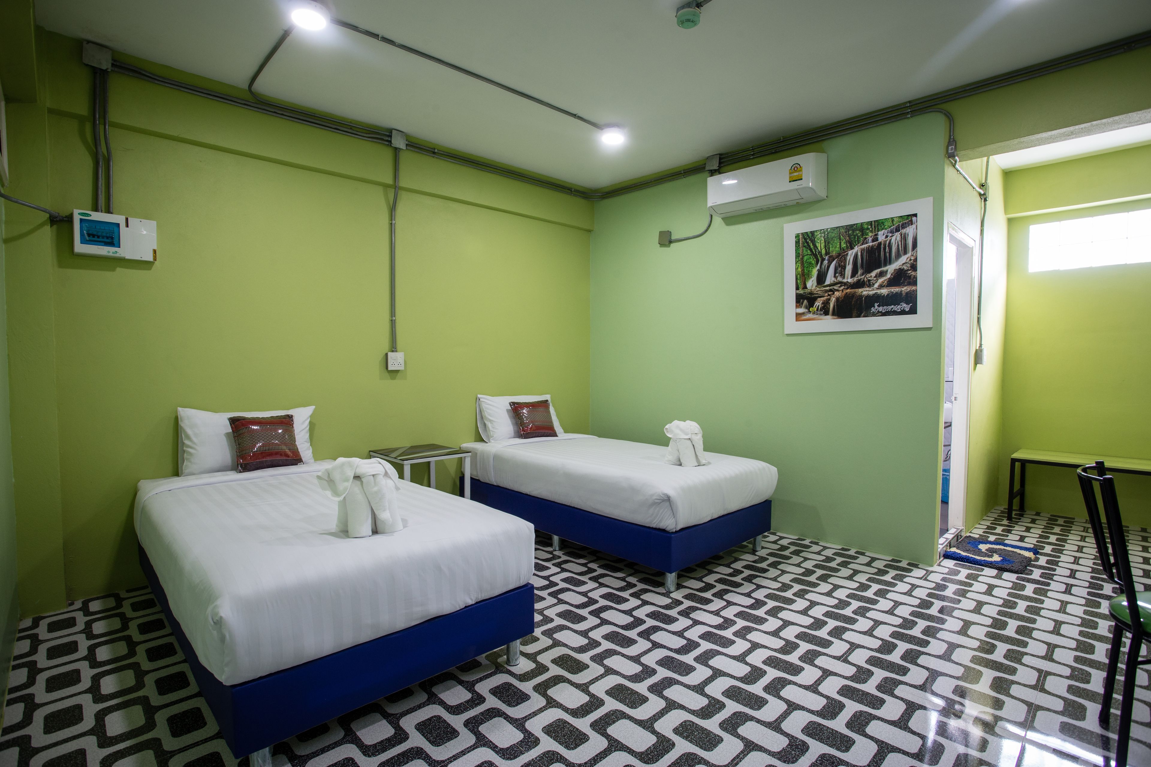 A room with two beds, a small table, and a chair. There is a picture on the wall and a window with a view of a waterfall.