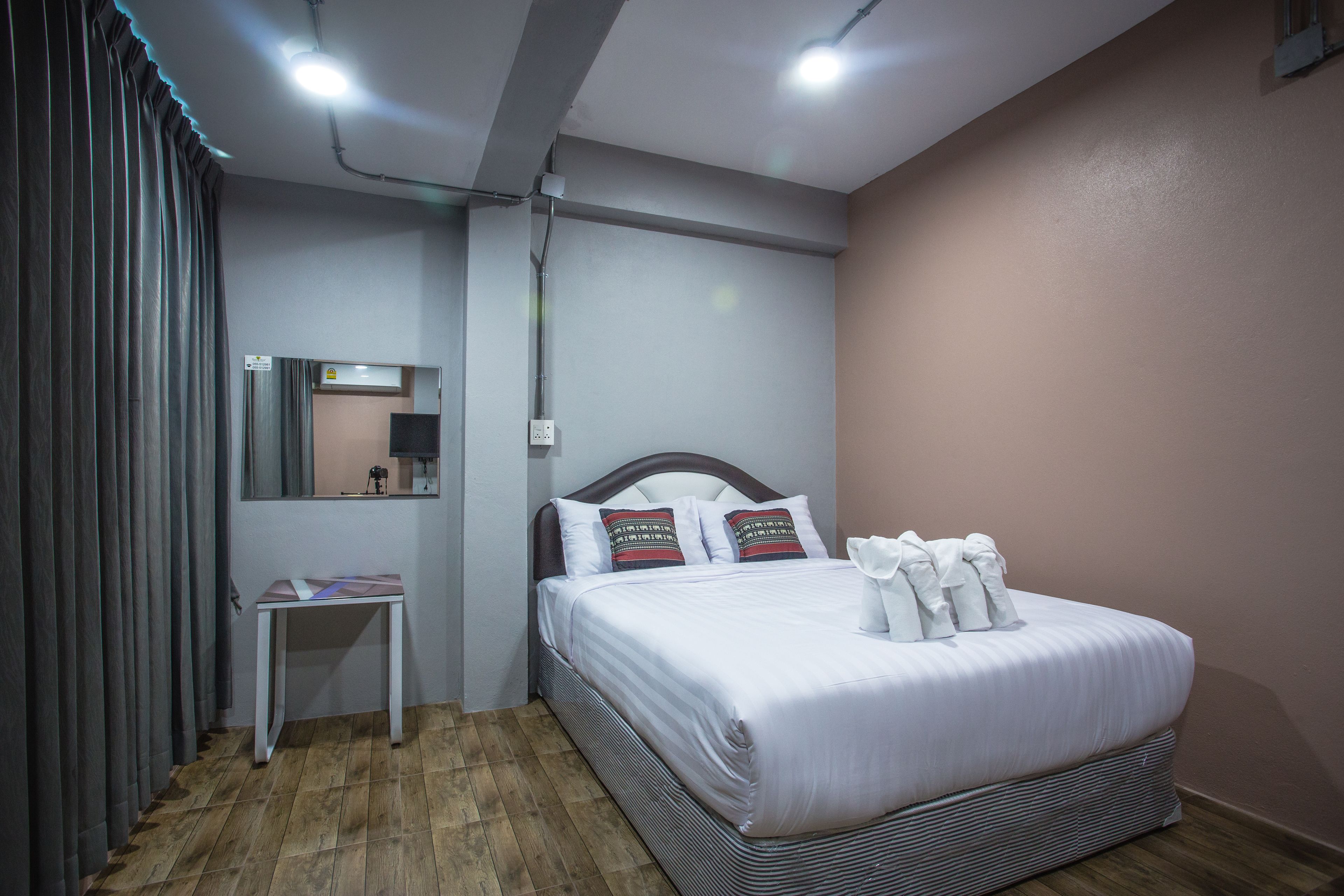 A neatly arranged bedroom with a bed, a bedside table, a mirror, and a window with curtains.