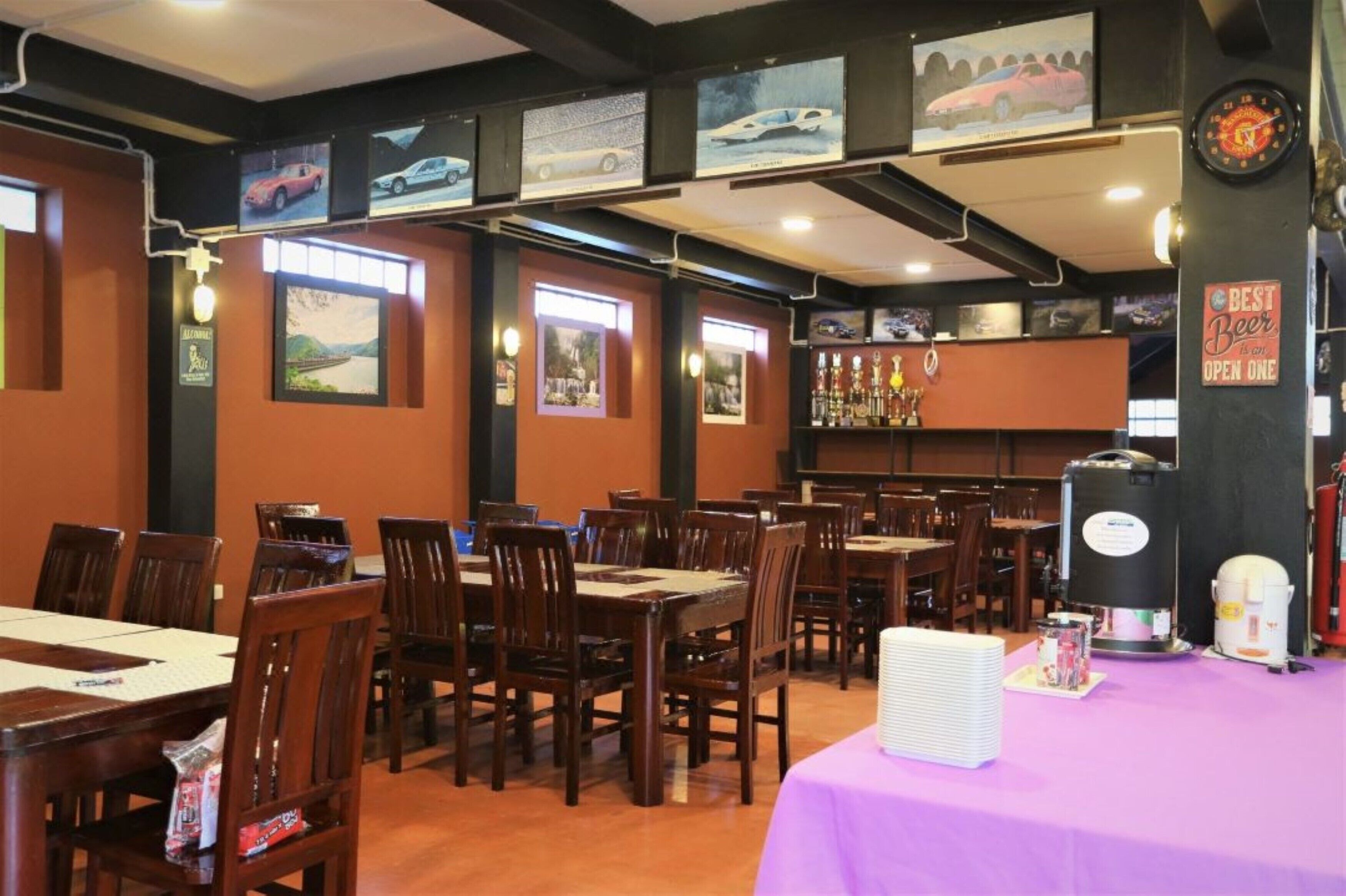 Un restaurant avec des tables et des chaises en bois, un coin bar avec des bouteilles exposées et des tableaux encadrés accrochés aux murs.