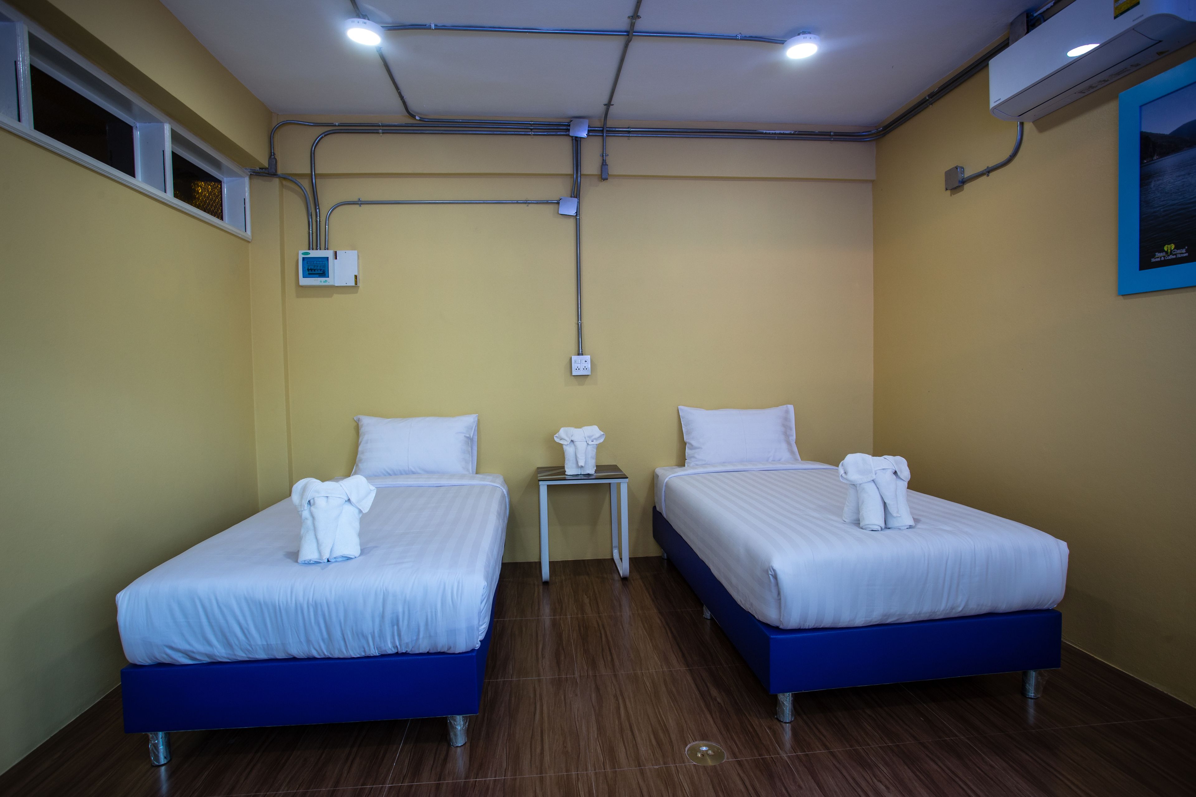 A hotel room with two beds, a small table, and an air conditioning unit on the wall.