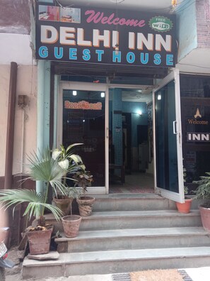 The entrance to Delhi Inn Guest House with a signboard, reception area, and potted plants.
