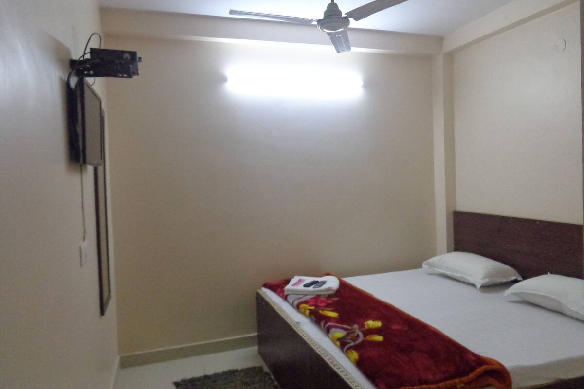 A single bed with a red blanket, white pillows, and a ceiling fan.