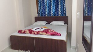 A single bed with a patterned blanket, a wooden headboard, and a blue patterned curtain. - Delhi Inn (New Delhi)