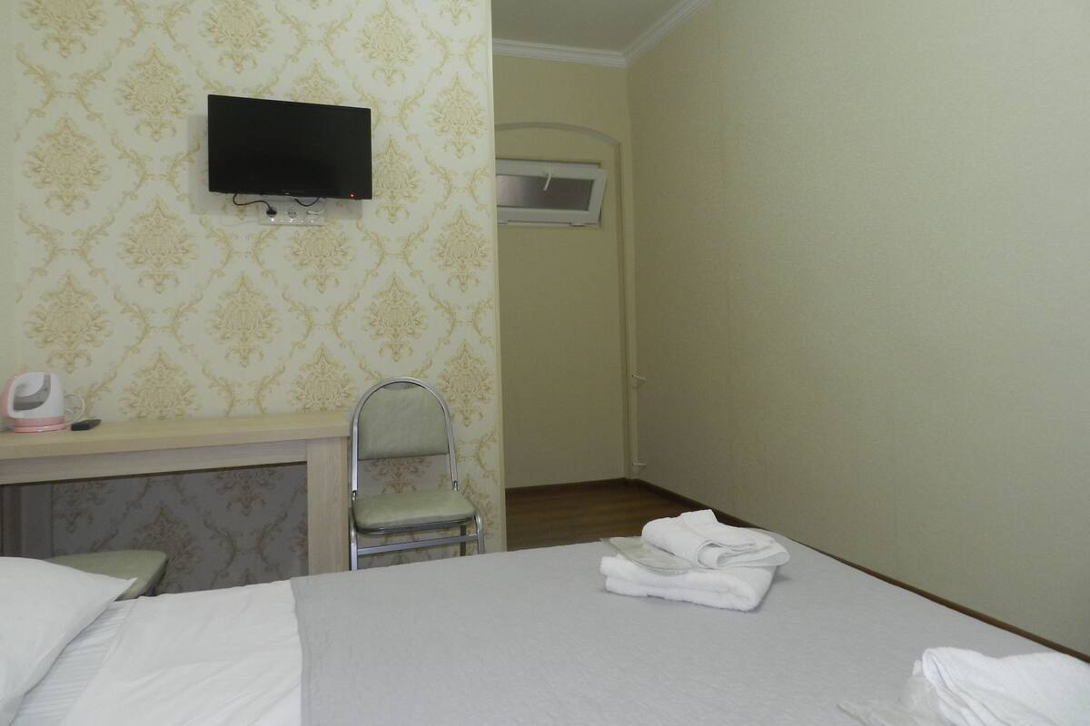 A hotel room with a bed, a TV mounted on the wall, a chair, and a folded towel on the bed.