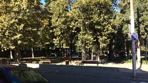 Une voiture rouge est garée dans une rue, avec un passage piéton et des arbres en arrière-plan.