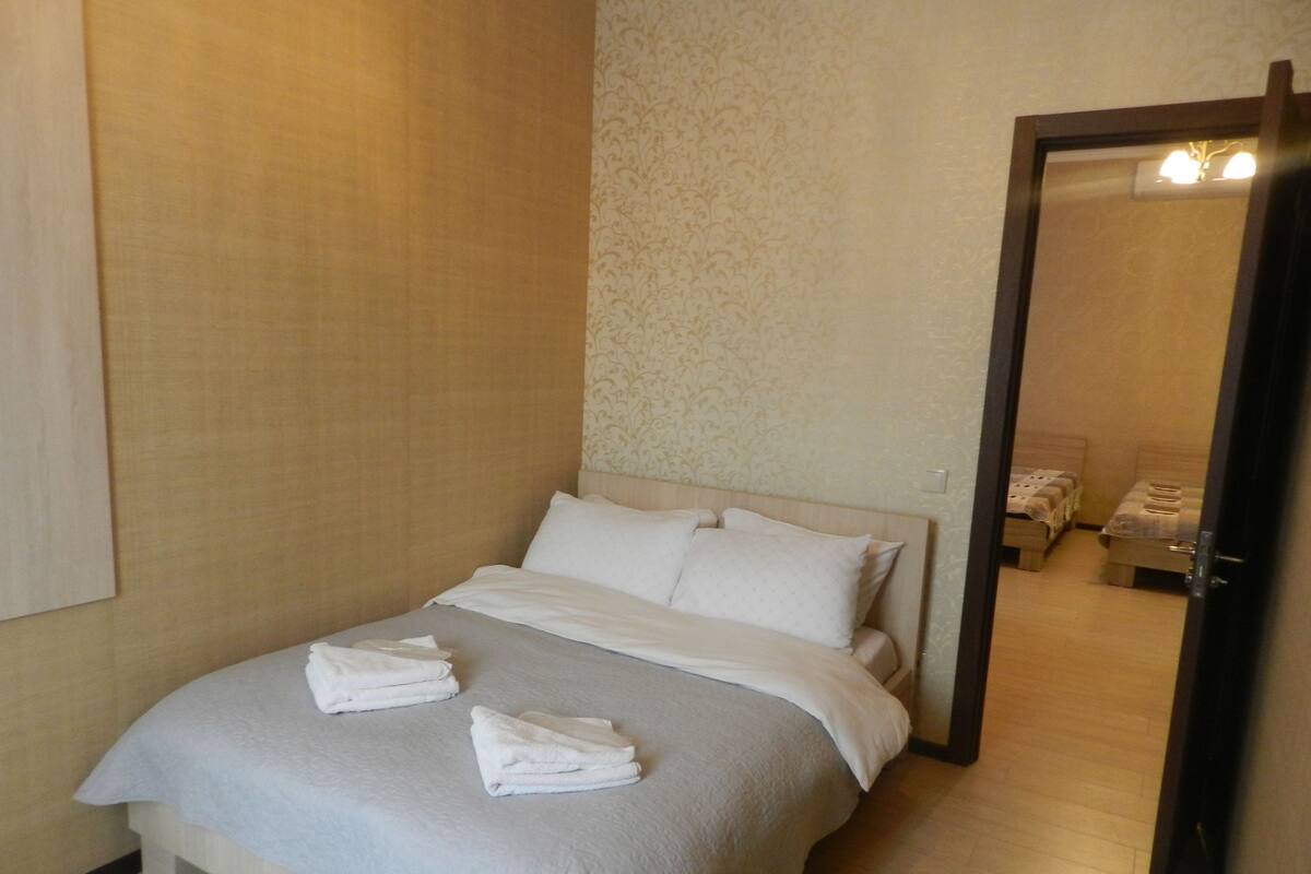 A neatly made bed with white linens and towels, a wooden headboard, and a patterned wallpaper on the wall.