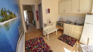 A compact kitchen with white cabinets, a microwave, and a sink. There is a small table and a colorful rug on the floor. - Tango - Apartments on the Beach (Corfu)