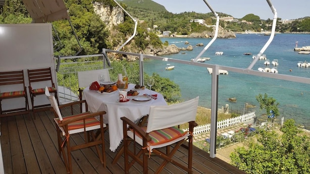 A wooden deck with a table set for dining, overlooking a coastal area with boats and greenery. - Tango - Apartments on the Beach (Corfu)