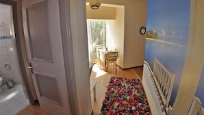 A hallway with a door leading to a bathroom, a colorful rug, and a dining area with a table and chairs. - Tango - Apartments on the Beach (Corfu)