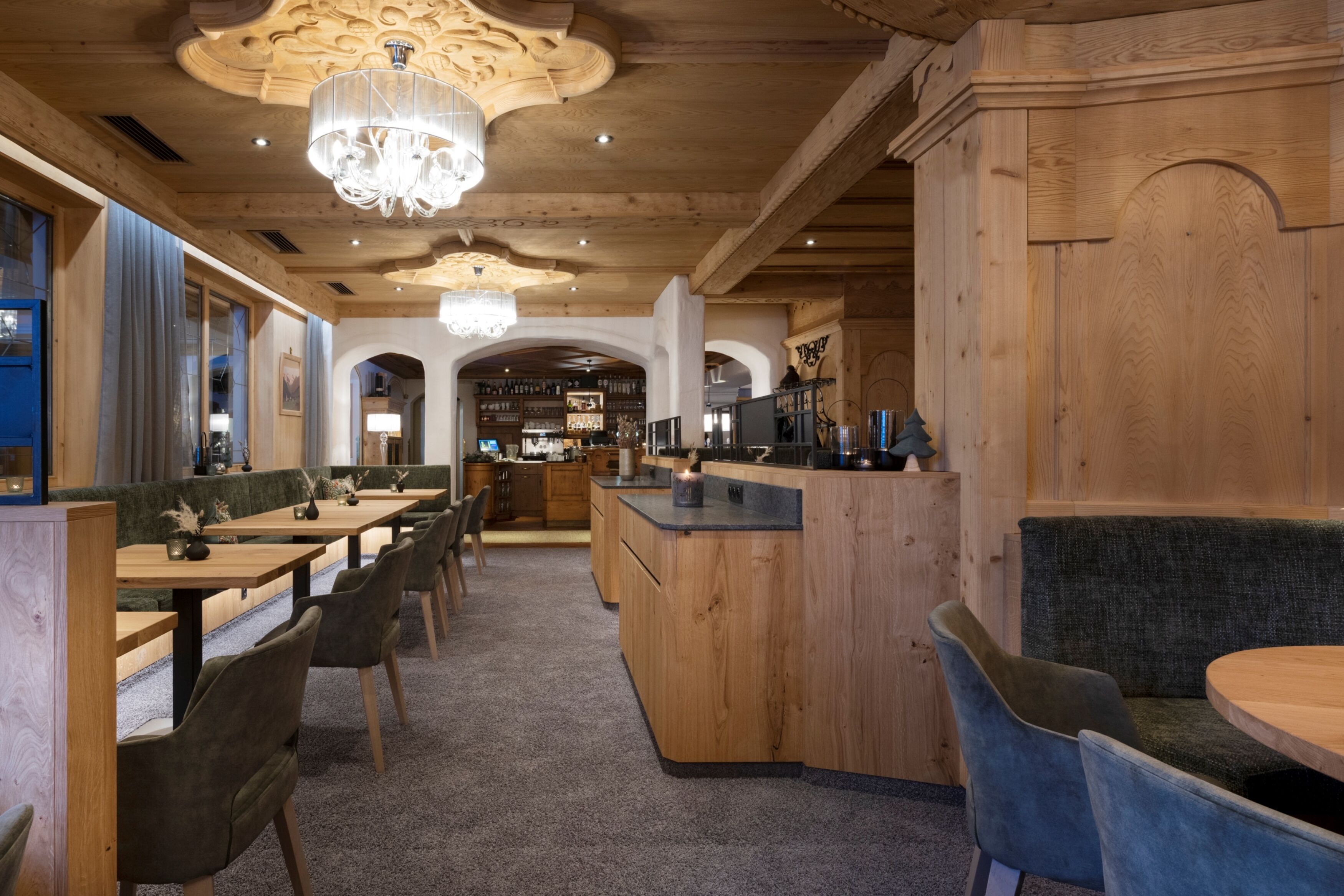 Een restaurantinterieur met houten tafels en stoelen, een bar en een kroonluchter.