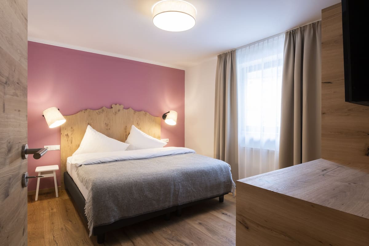 Une chambre d’hôtel moderne avec un lit en bois, une petite table de chevet et une grande fenêtre avec des rideaux.