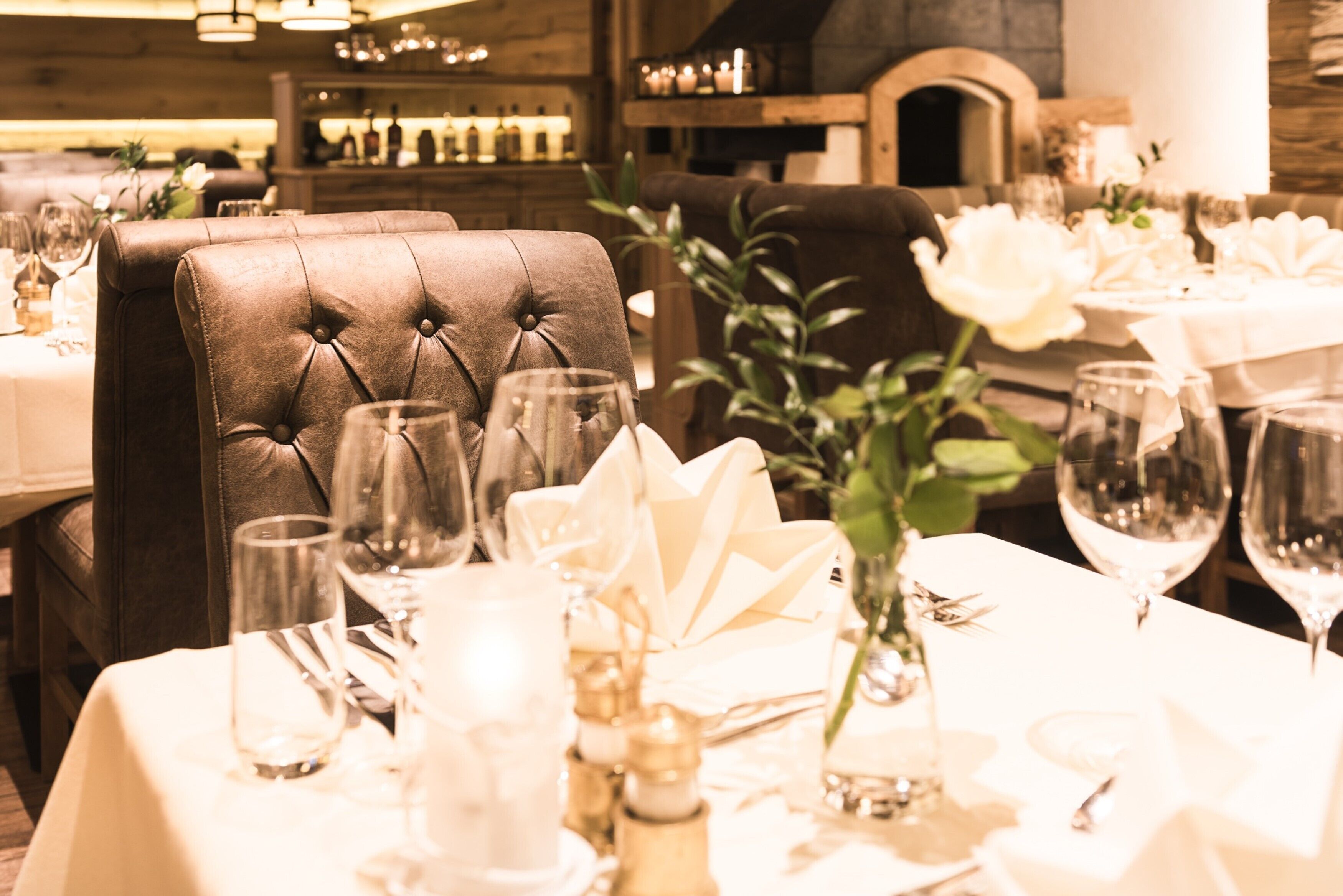 Una mesa de comedor con manteles blancos, copas de vino y un centro de mesa con una rosa blanca.