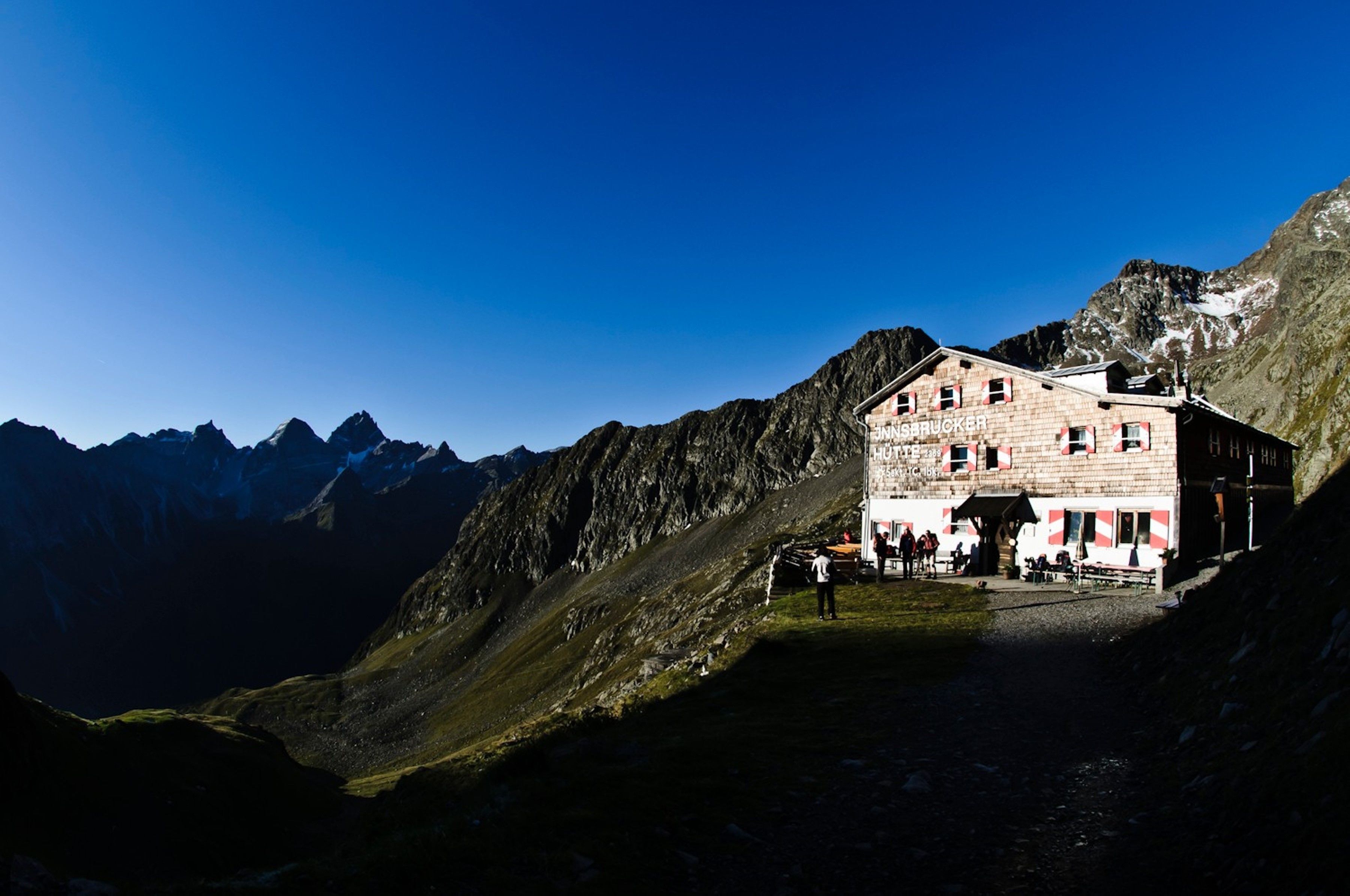 A mountain lodge with a red and white facade, situated in a valley with steep mountain slopes.
