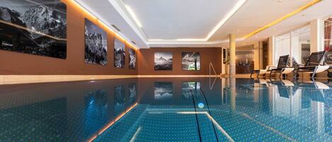 A modern indoor swimming pool with a clear blue floor, surrounded by walls with framed photographs.