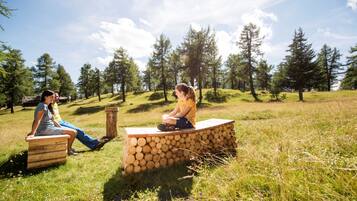Dos personas sentadas en bancos de madera en un campo cubierto de hierba, con árboles al fondo.
