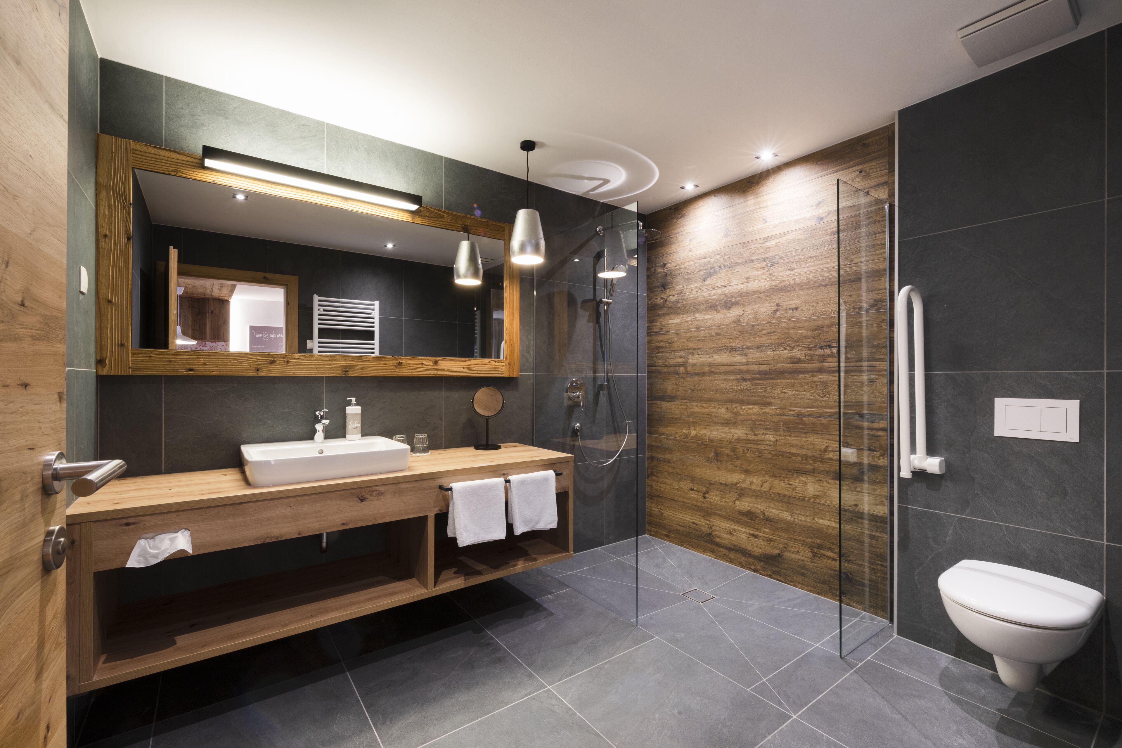 Une salle de bain moderne avec un meuble-lavabo en bois, un grand miroir, une douche en verre et des toilettes.