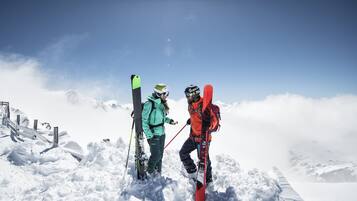 Zwei Skifahrer auf einem verschneiten Berg unter blauem Himmel.