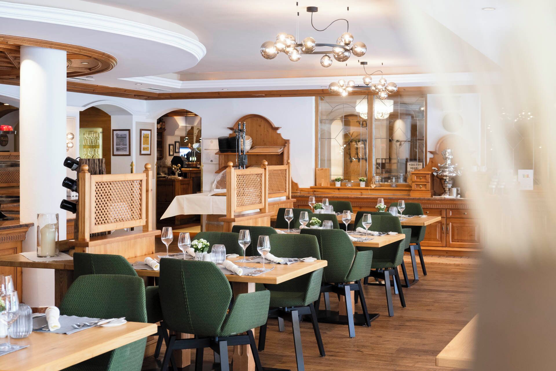 Een restaurant met houten tafels en stoelen, een kroonluchter en een spiegel aan de muur.