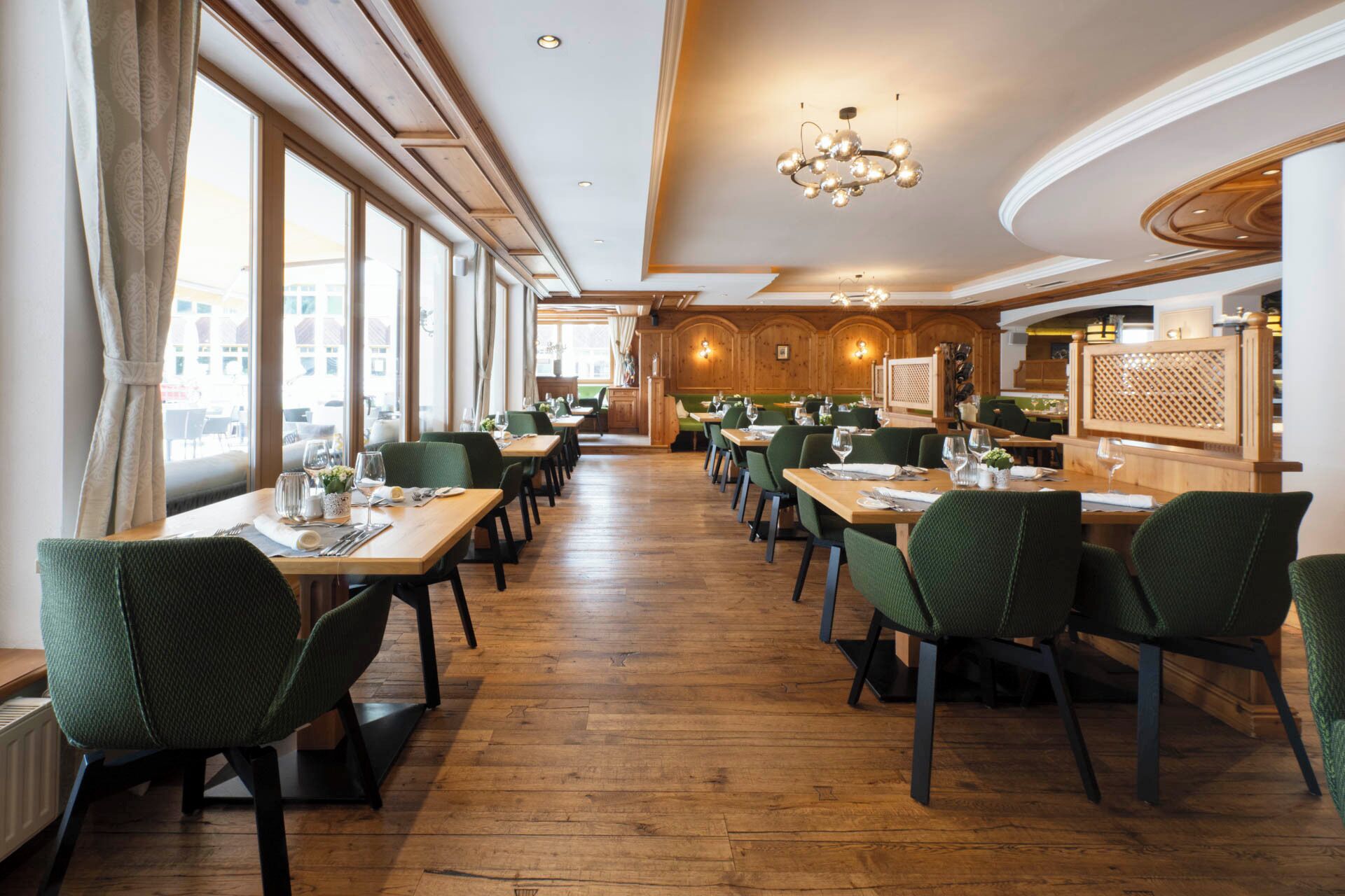 Een restaurant met houten vloeren, groene beklede stoelen en gedekte tafels.