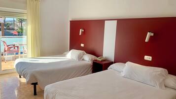 A hotel room with two beds, a red accent wall, a small bedside table with a phone, and a view of a pool and outdoor seating.