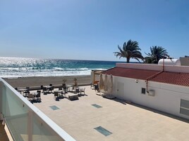 A rooftop terrace with outdoor seating, a view of the ocean, and palm trees.