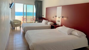 Een hotelkamer met twee bedden, een bureau, een stoel en uitzicht op zee.