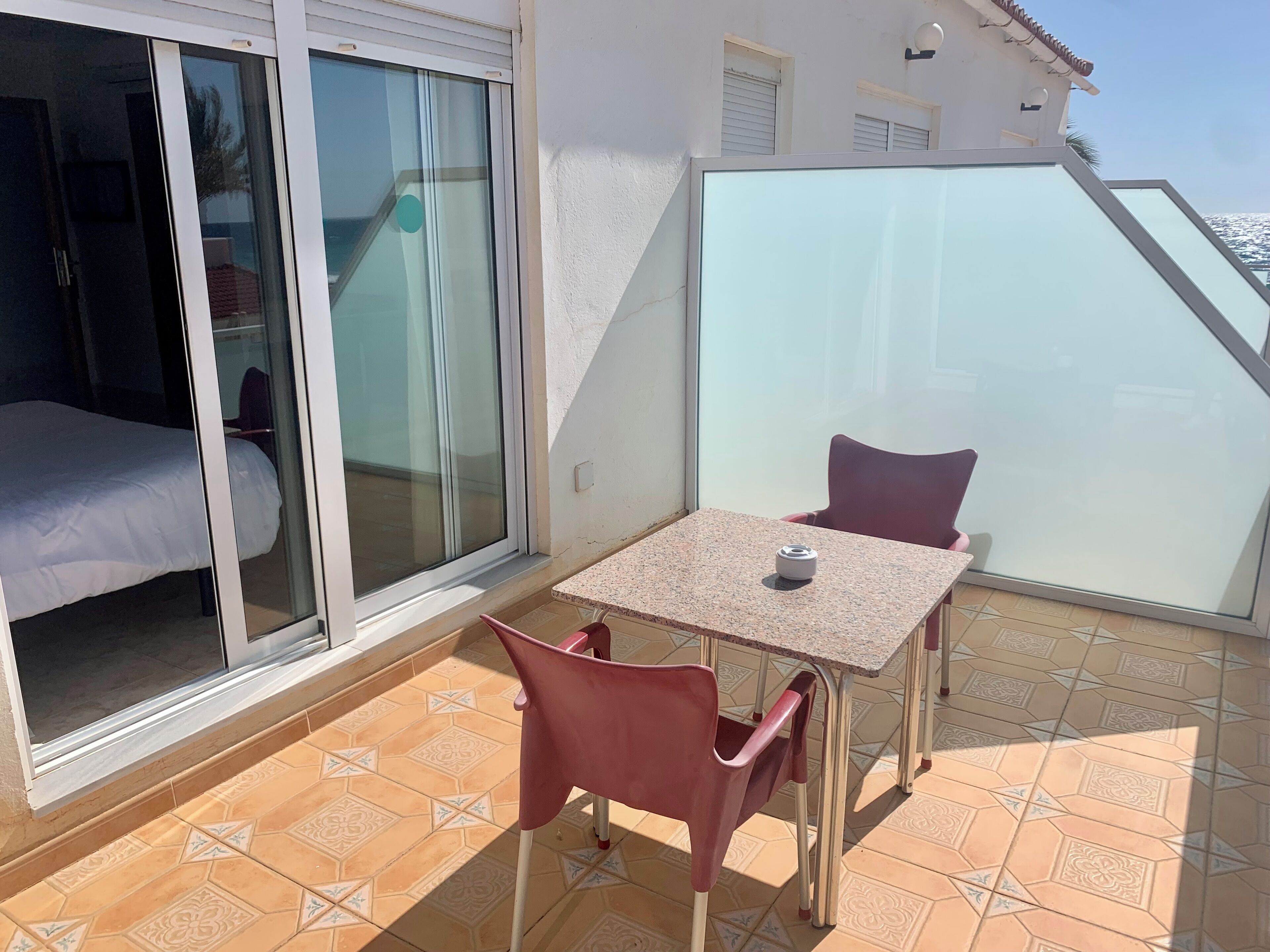 A balcony with a table and chairs, a bed, and a sliding glass door.