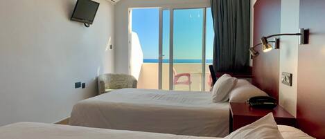 A hotel room with two beds, a TV, a desk with a phone, and a view of the sea.