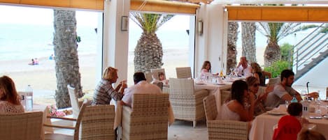 An outdoor dining area with wicker chairs and tables, overlooking a beach.