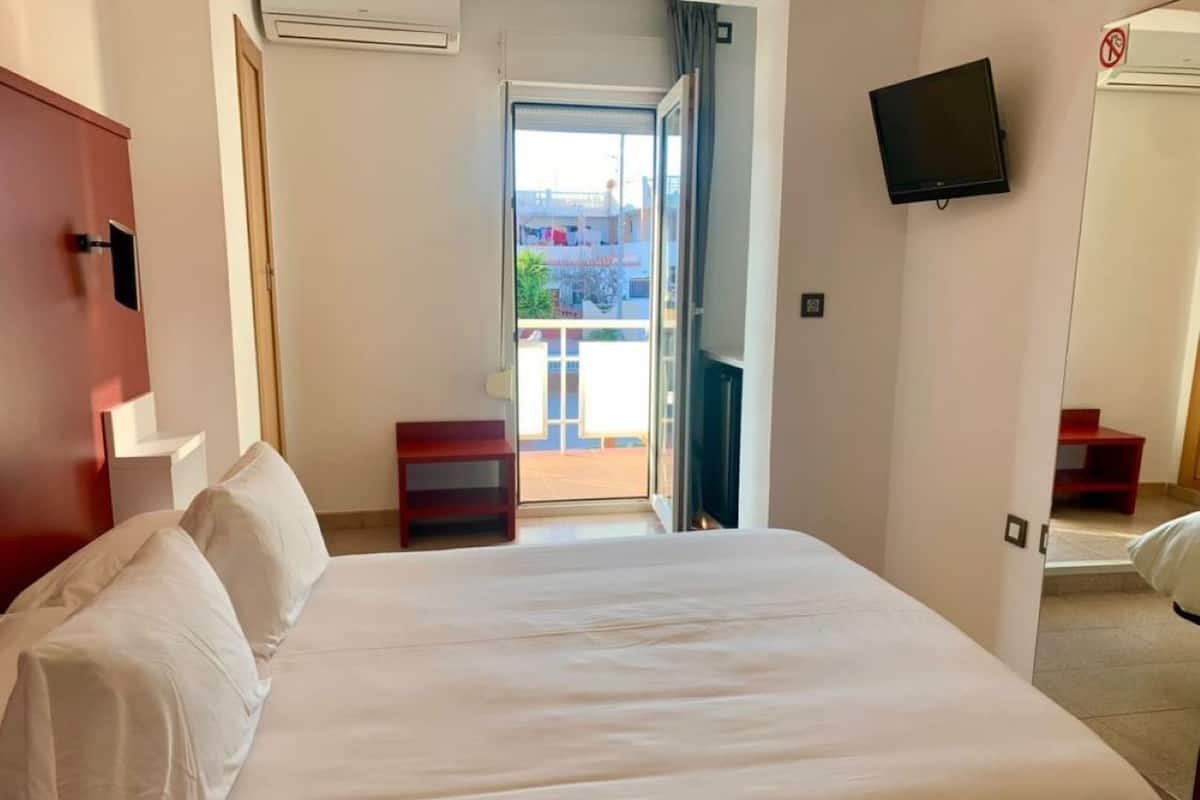 A hotel room with a large bed, a TV mounted on the wall, and a view of the outside balcony.