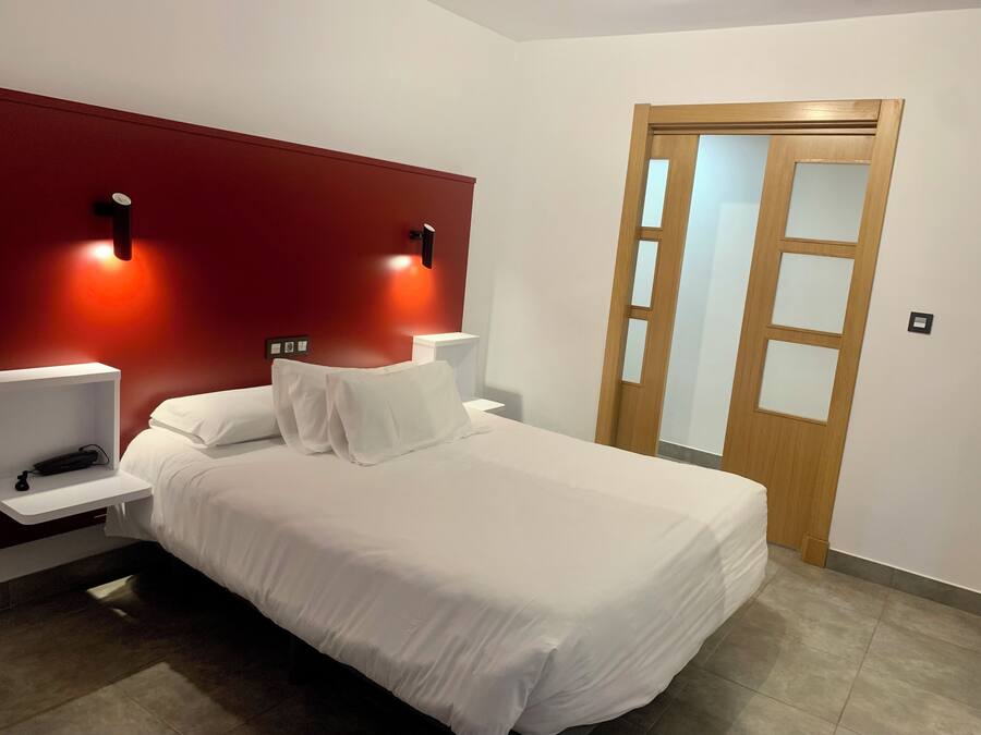 Een net opgemaakt bed met witte lakens in een moderne kamer met een rode accentmuur en twee bedlampjes.