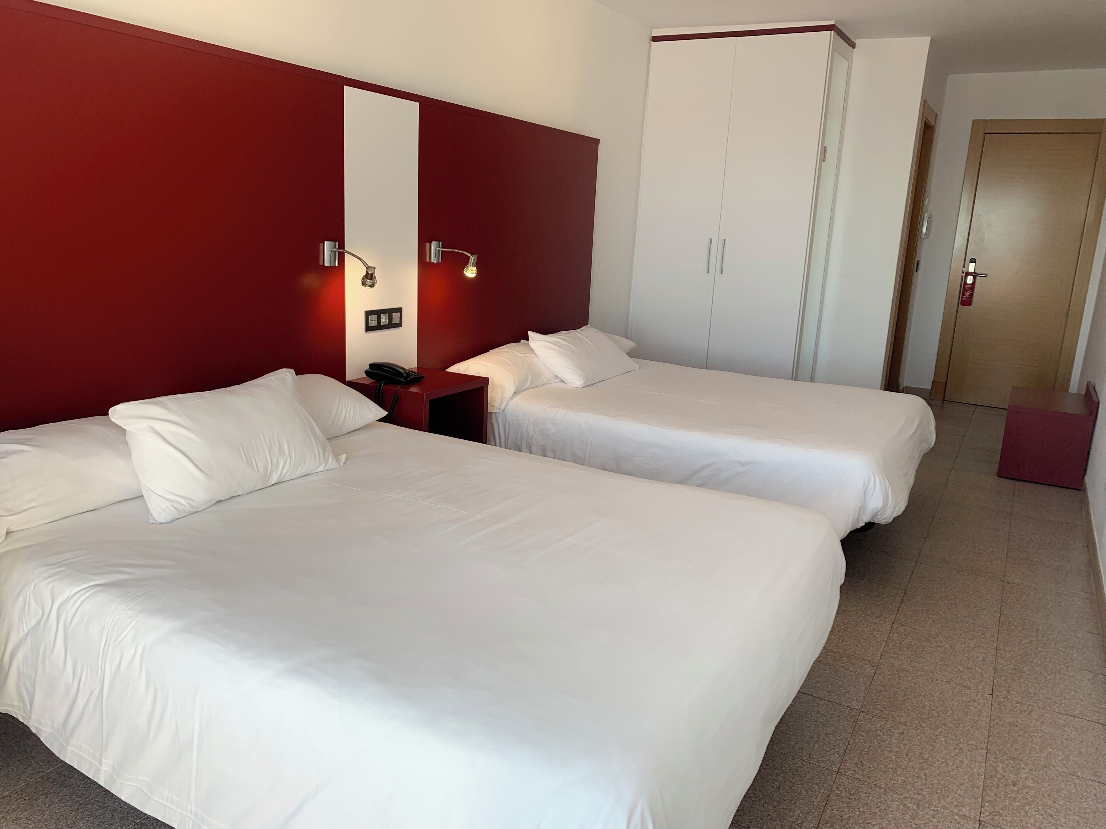 Ett hotellrum med två sängar, en röd accentvägg, en garderob och ett nattduksbord med en telefon.