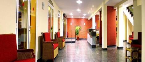 Una hall d'albergo con una reception, posti a sedere imbottiti di colore rosso e una scala.