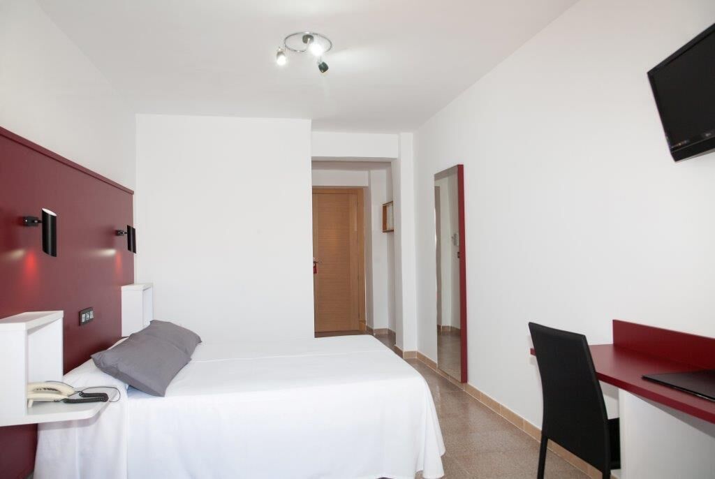 Hotelkamer met een bed, nachtkastje, lamp, bureau, stoel en een aan de muur bevestigde televisie.