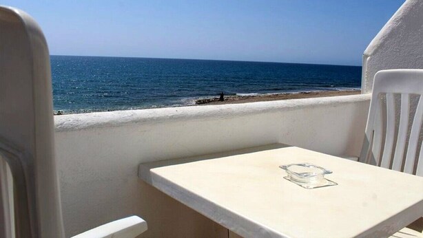 Een balkon met tafel en stoelen met uitzicht op een strand.