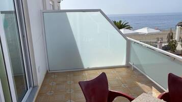 Un balcon avec une table et des chaises, donnant sur une plage et la mer.