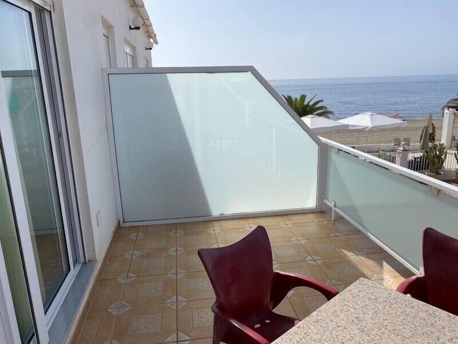 Un balcon avec une table et des chaises, donnant sur une plage et la mer.