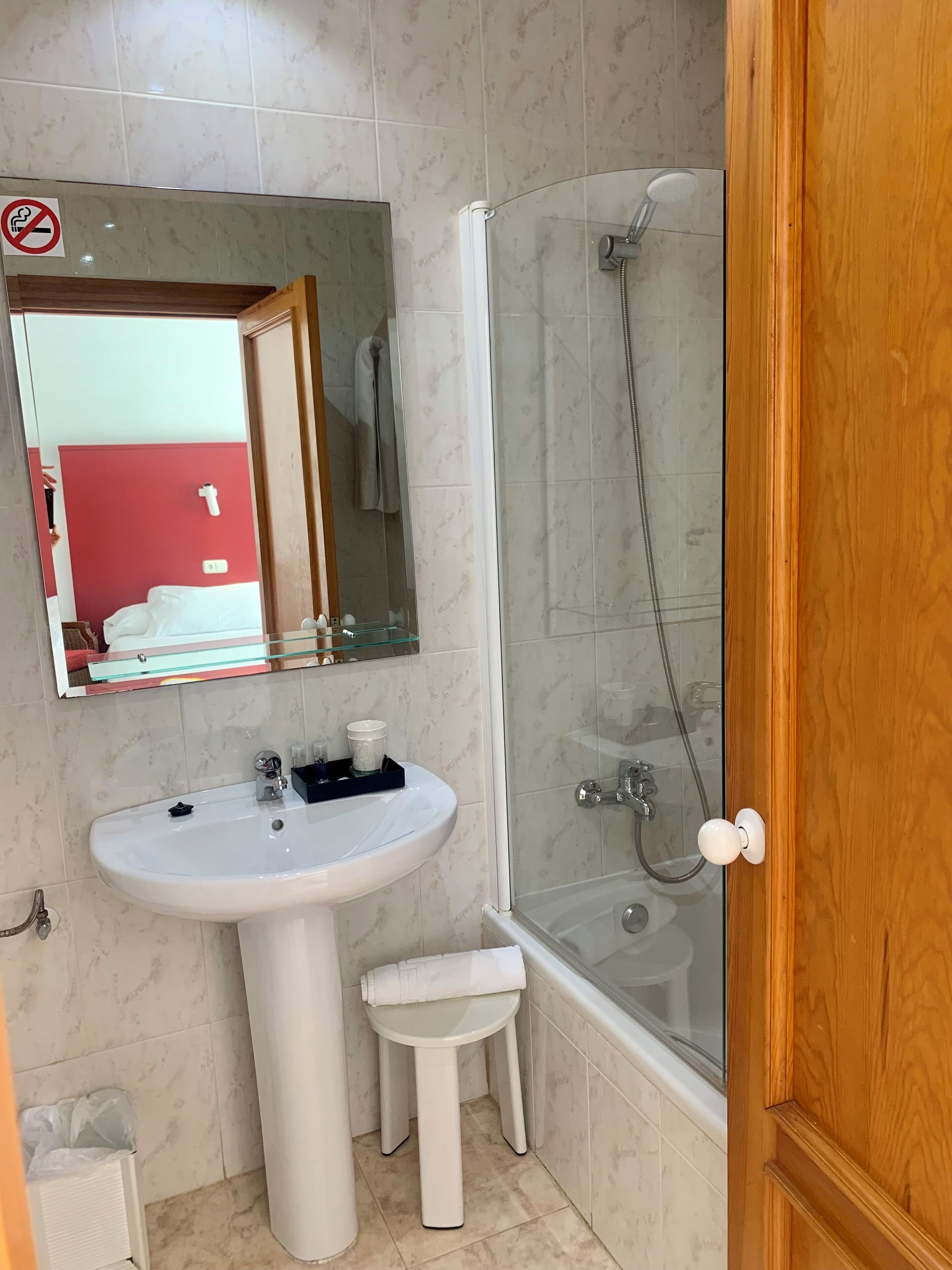 A bathroom with a white sink, a mirror, a glass shower enclosure, and a wooden door.
