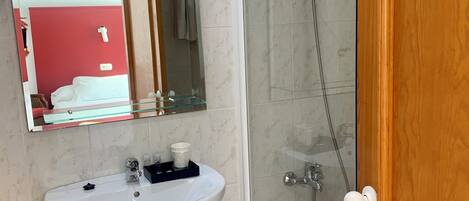 Un baño con lavamanos blanco, un espejo, cabina de ducha de vidrio y puerta de madera.